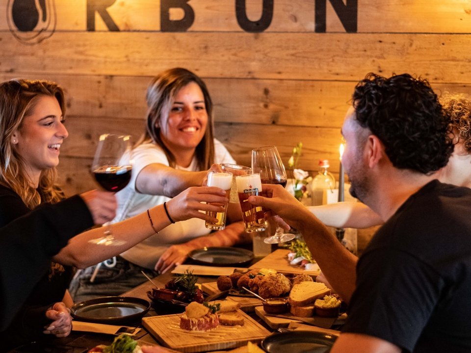 Gasten proosten met bier en wijn aan een houten tafel onder de CARBON-wand